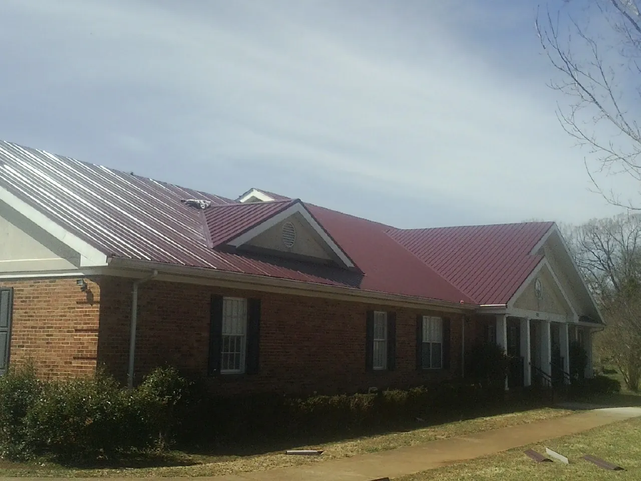 Red metal roof with gabled entries on a long brick building, from a Hail Damage Roof Repair job in McMinnville