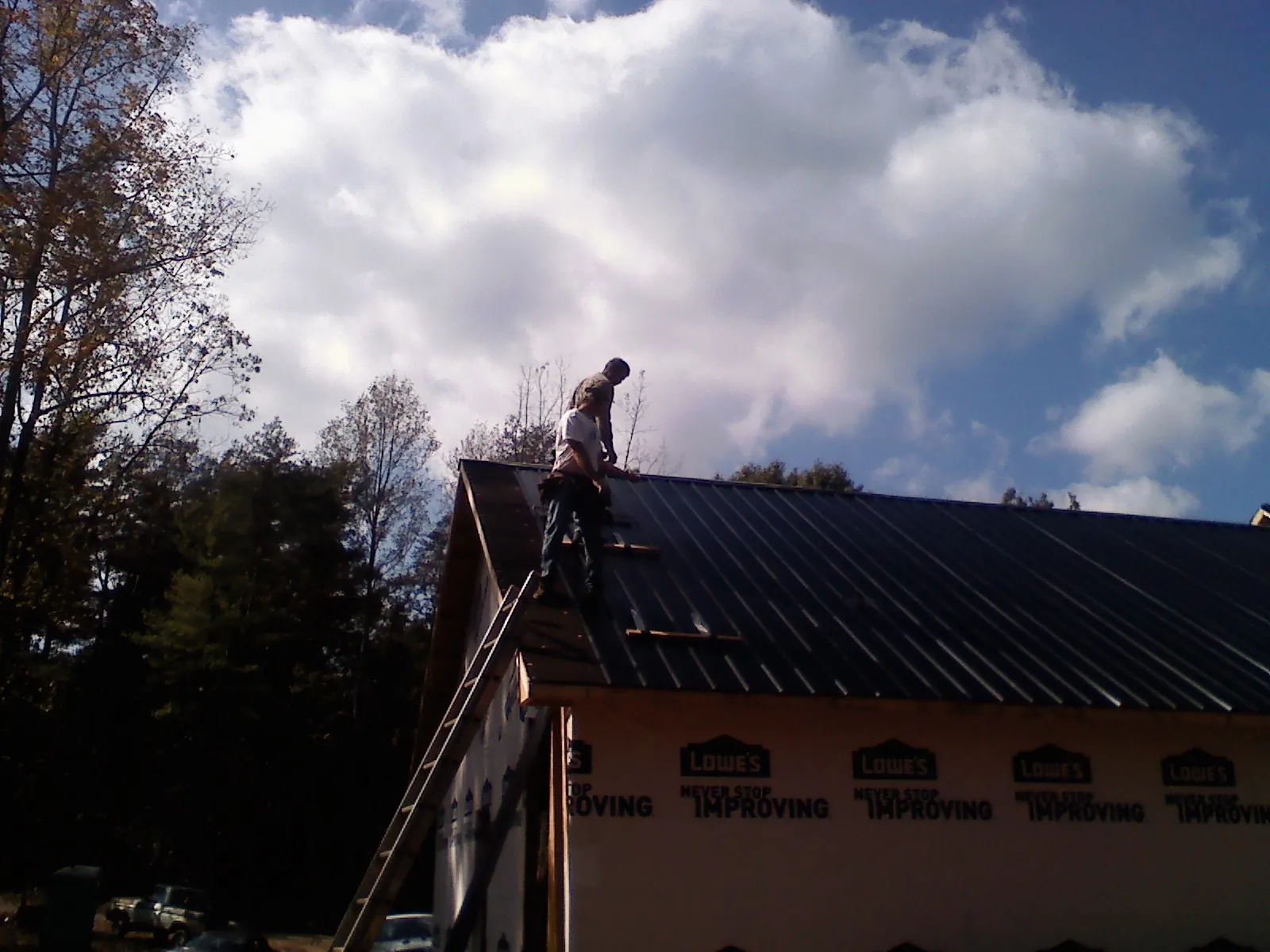 Roofer fastening dark metal panels high against a cloudy sky, from a Roof Inspection job in McMinnville